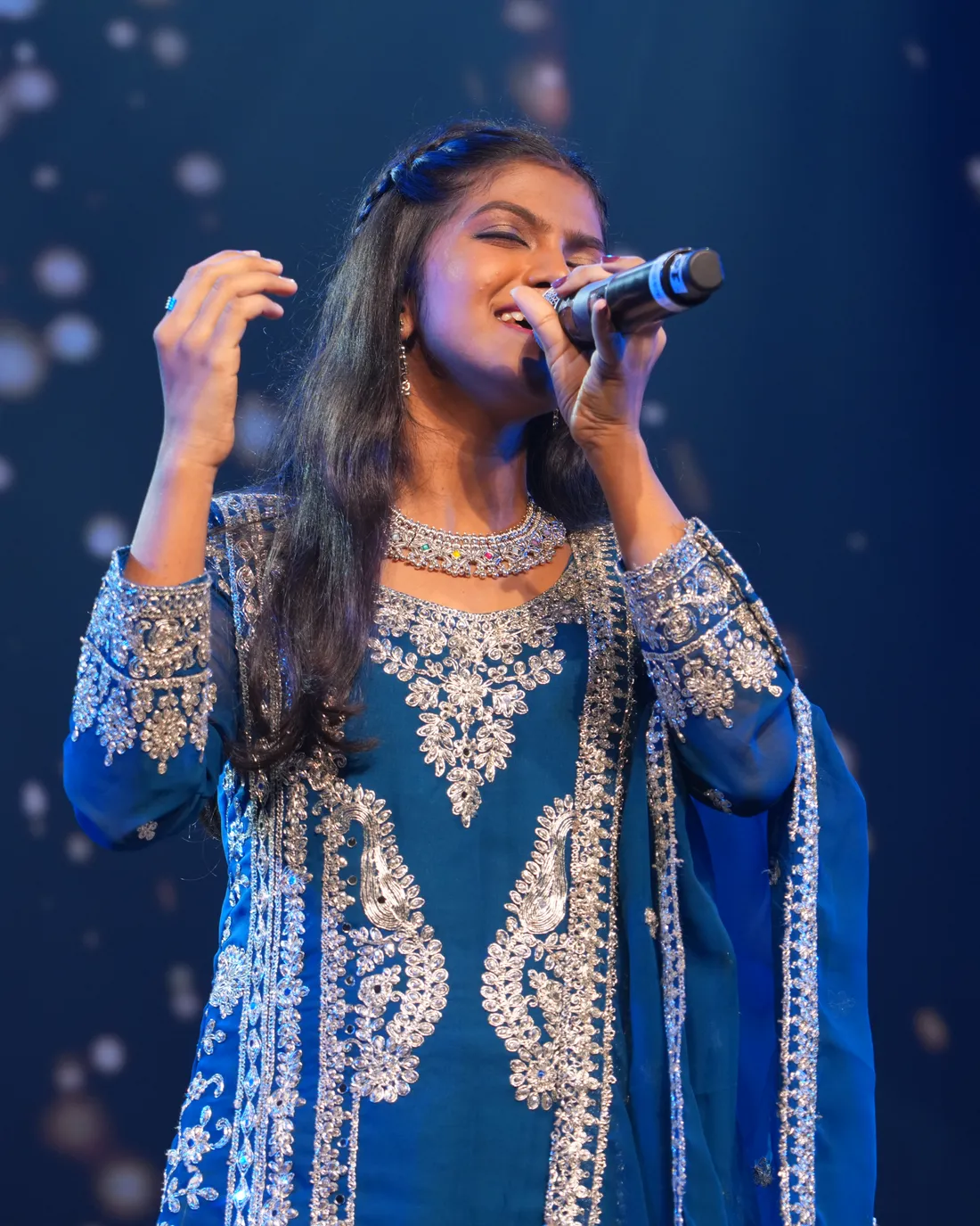 An Artium learner singing on stage under falling lights