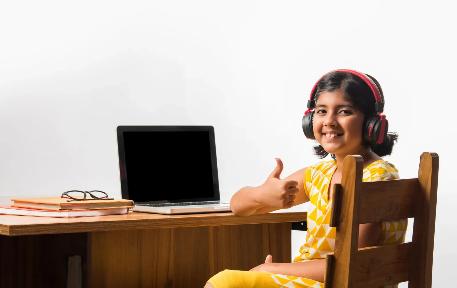 A young learner in headphones giving a thumbs up during her live class