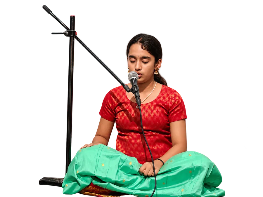 An Artium learner singing Carnatic music at a microphone, seated on stage