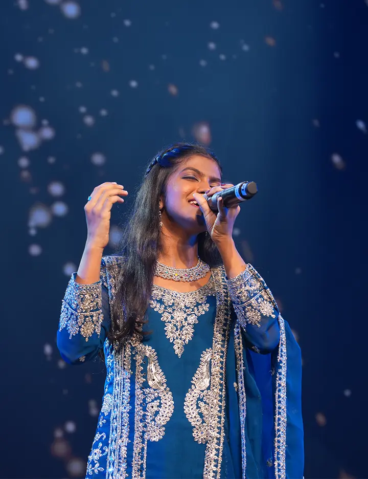 An Artium learner singing on stage under falling lights