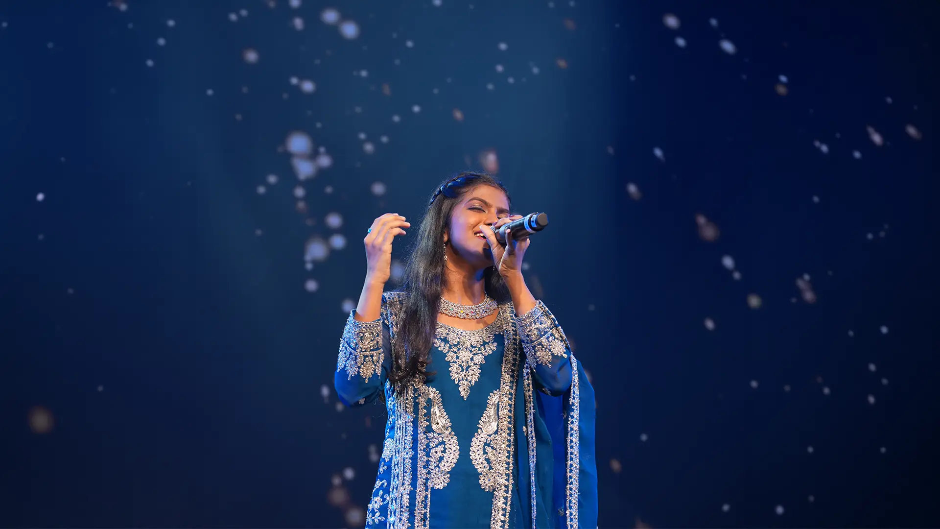 An Artium learner singing on stage under falling lights